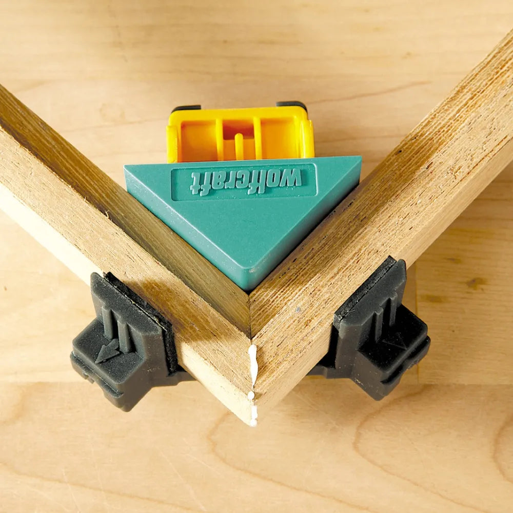 Una prensa wolfcraft en primer plano, sujetando y uniendo dos piezas de madera en un ángulo de 90 grados