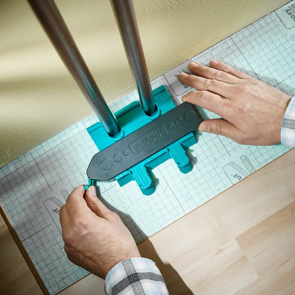 Calibre para contornos puesto sobre dos tubos de metal para copiar su forma y realizar el corte perfecto en el piso flotante