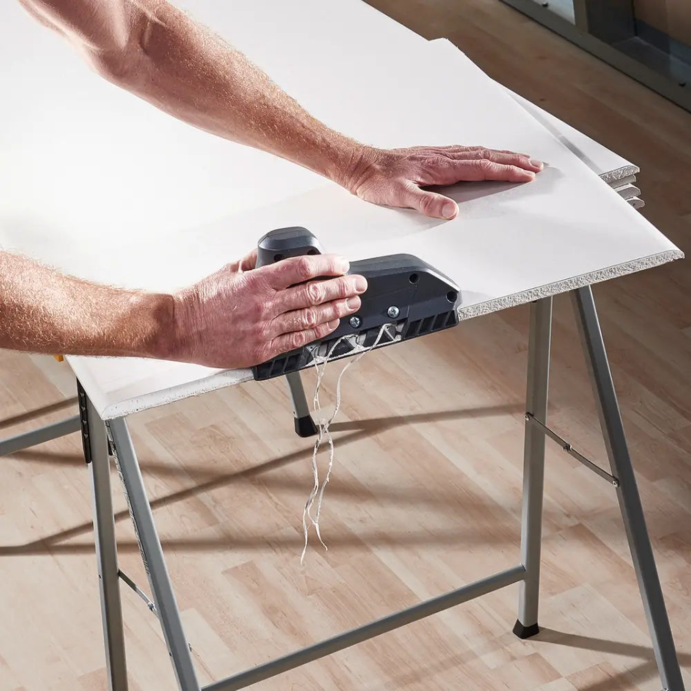 En primer plano, la canteadora cortando el borde de una placa de yeso sobre un caballete y dejando un ángulo perfecto de 35 grados