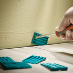 Dos cuñas unidas siendo colocadas con un atornillador como distanciadores entre la pared y el piso flotante